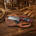 Handmade bull cutter knife with rasp steel blade epoxy resin handle and leather sheath on rustic wooden barn table