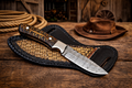 Cowboy hunting sheath knife with 4 inch Damascus steel blade and pinecone handle on rustic wooden table with cowboy rope and hat