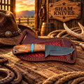 D2 Western skinner knife with a lacewood and turquoise handle resting on a tooled leather sheath
