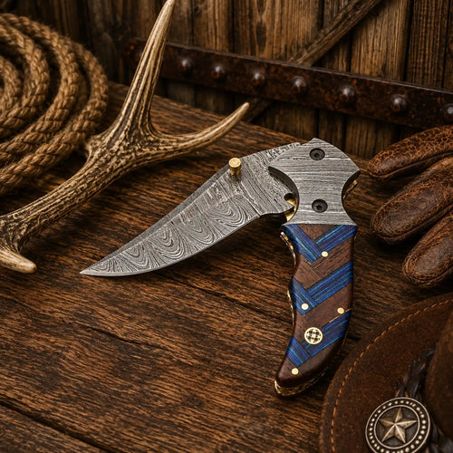 Handmade Western EDC folding knife with Damascus steel blade, Damascus bolsters, compact wood handle with blue accents, and leather belt sheath.