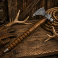 Handmade Damascus steel tomahawk with smokey hardwood handle displayed on a rustic wooden table.
